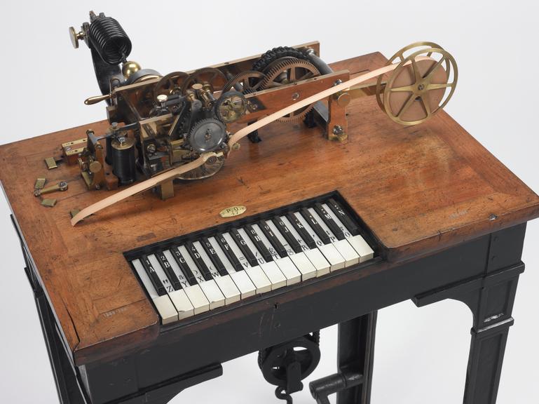 Photo du télégraphe de hughes, présentant un clavier comme un piano, avec des touches noires et blanches, mais avec des lettres dessus